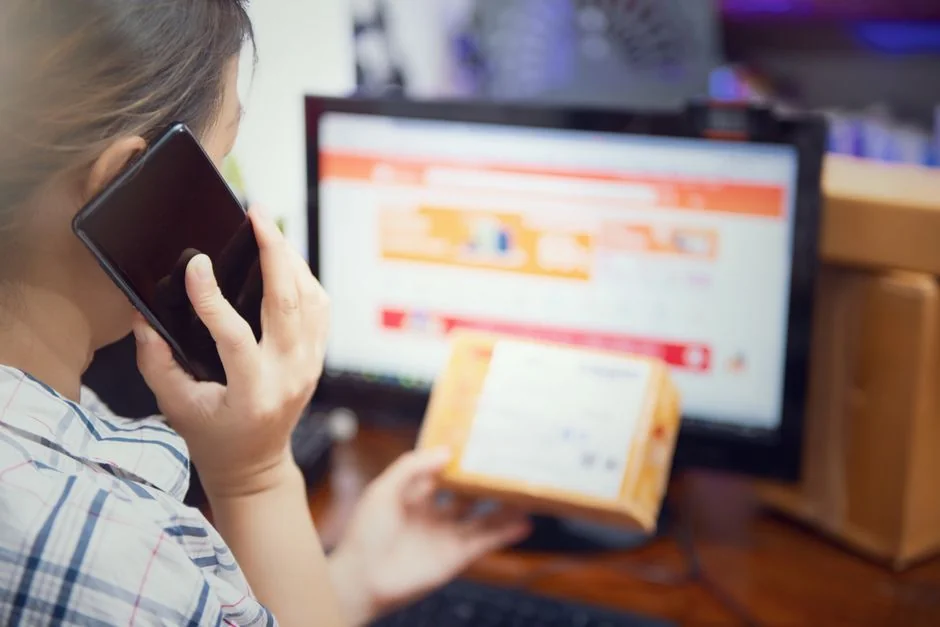 Hands using smartphone beside laptop with stock charts, showcasing digital trading.
